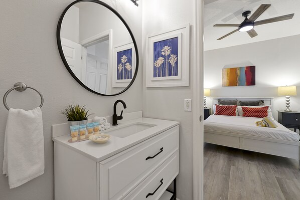 A modern bathroom with a white vanity, a round mirror, and a ceiling fan. - Vacation Townhomes by IDILIQ at Encantada Resort (Kissimmee)
