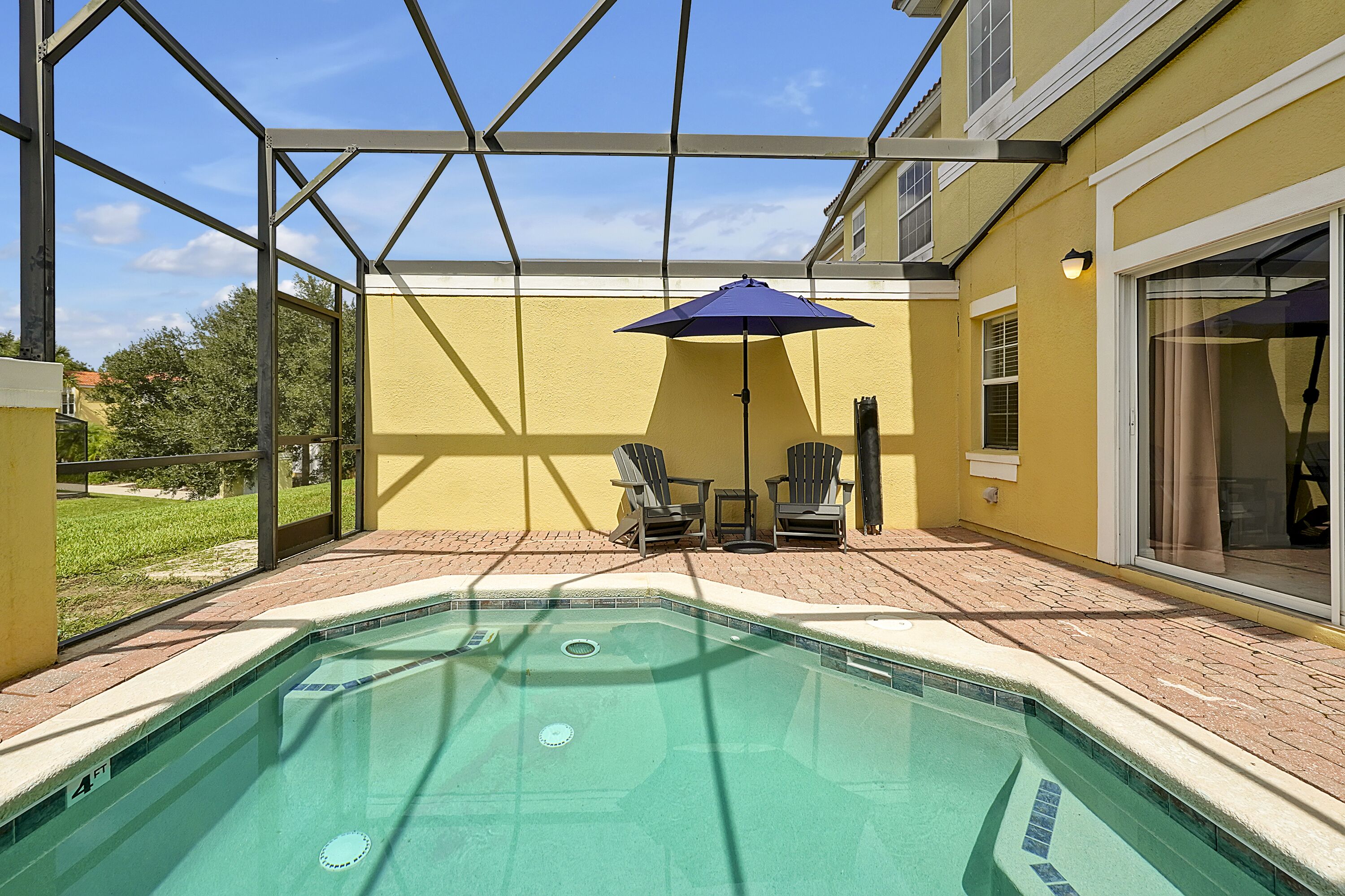 A swimming pool with a glass enclosure, a patio area with chairs, and an umbrella.