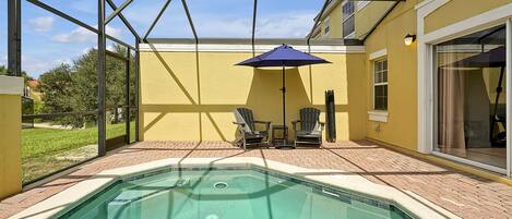 A swimming pool with a glass enclosure, a patio area with chairs, and an umbrella.