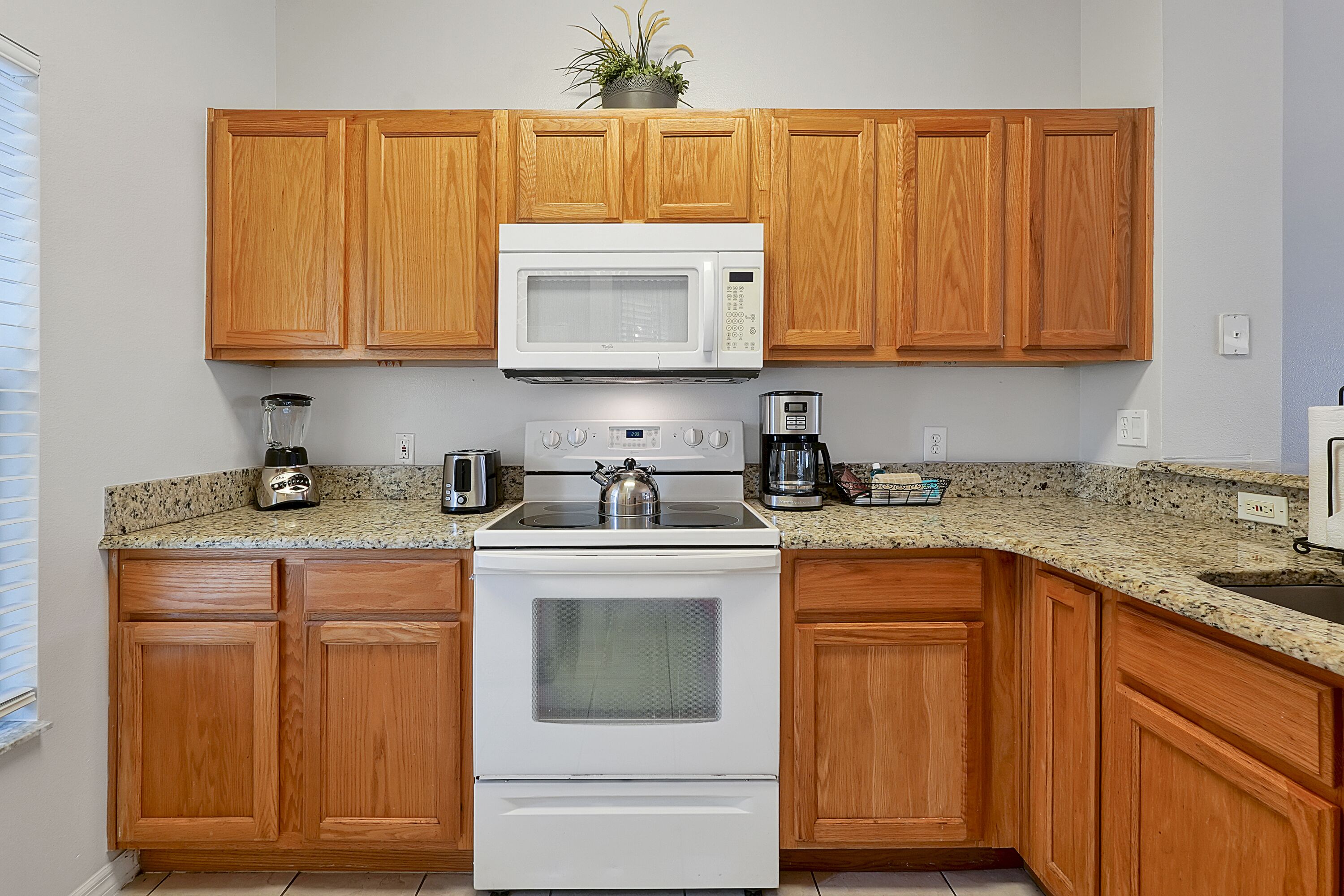 A kitchen with wooden cabinets, a white microwave, a stove, a blender, and a coffee maker.