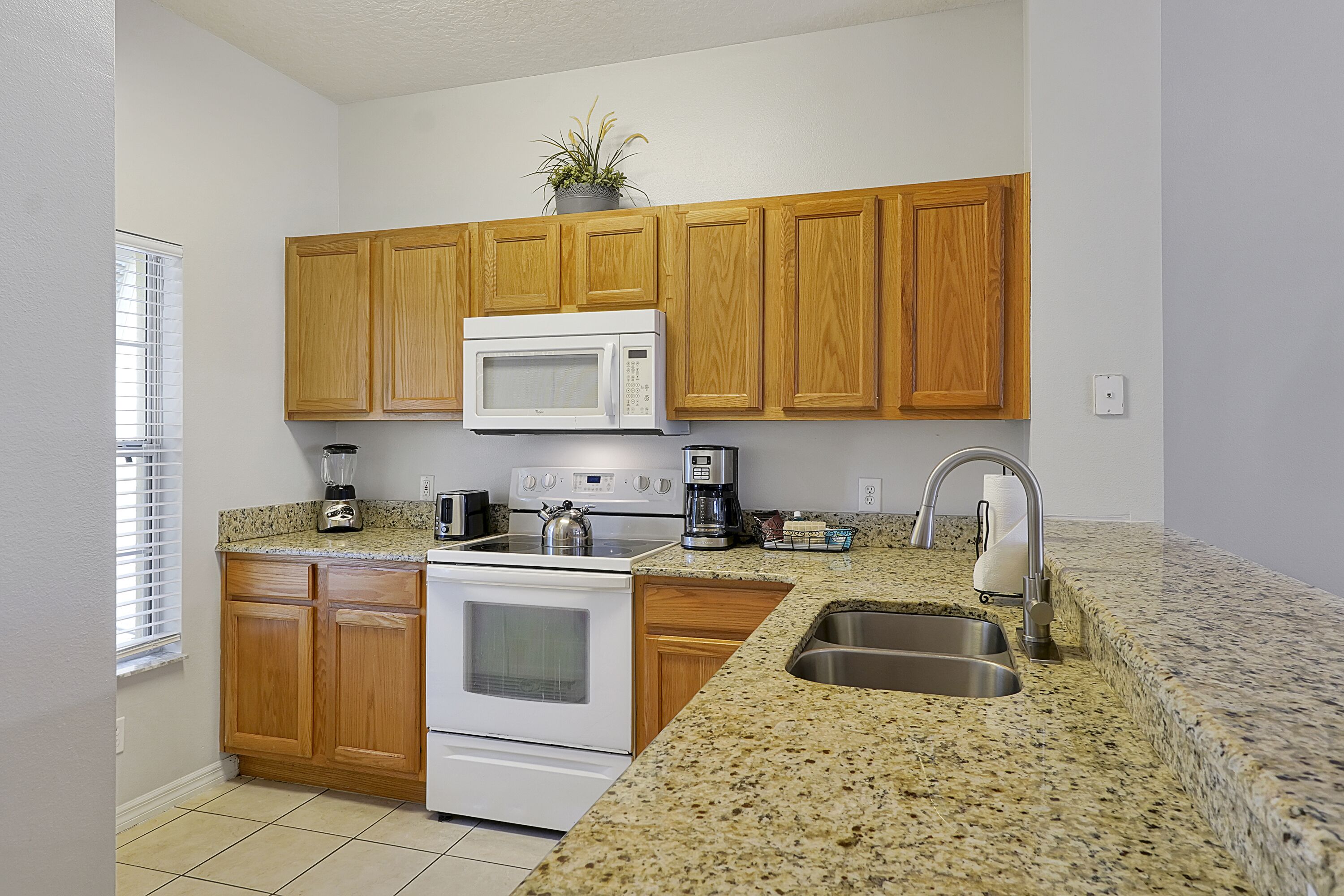 A kitchen with wooden cabinets, a white microwave, a stove, a sink, and a countertop with a plant.