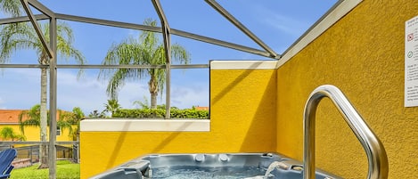 Een hottub met een metalen kraan, voor een gele muur, met zicht op palmbomen en een blauwe lucht.