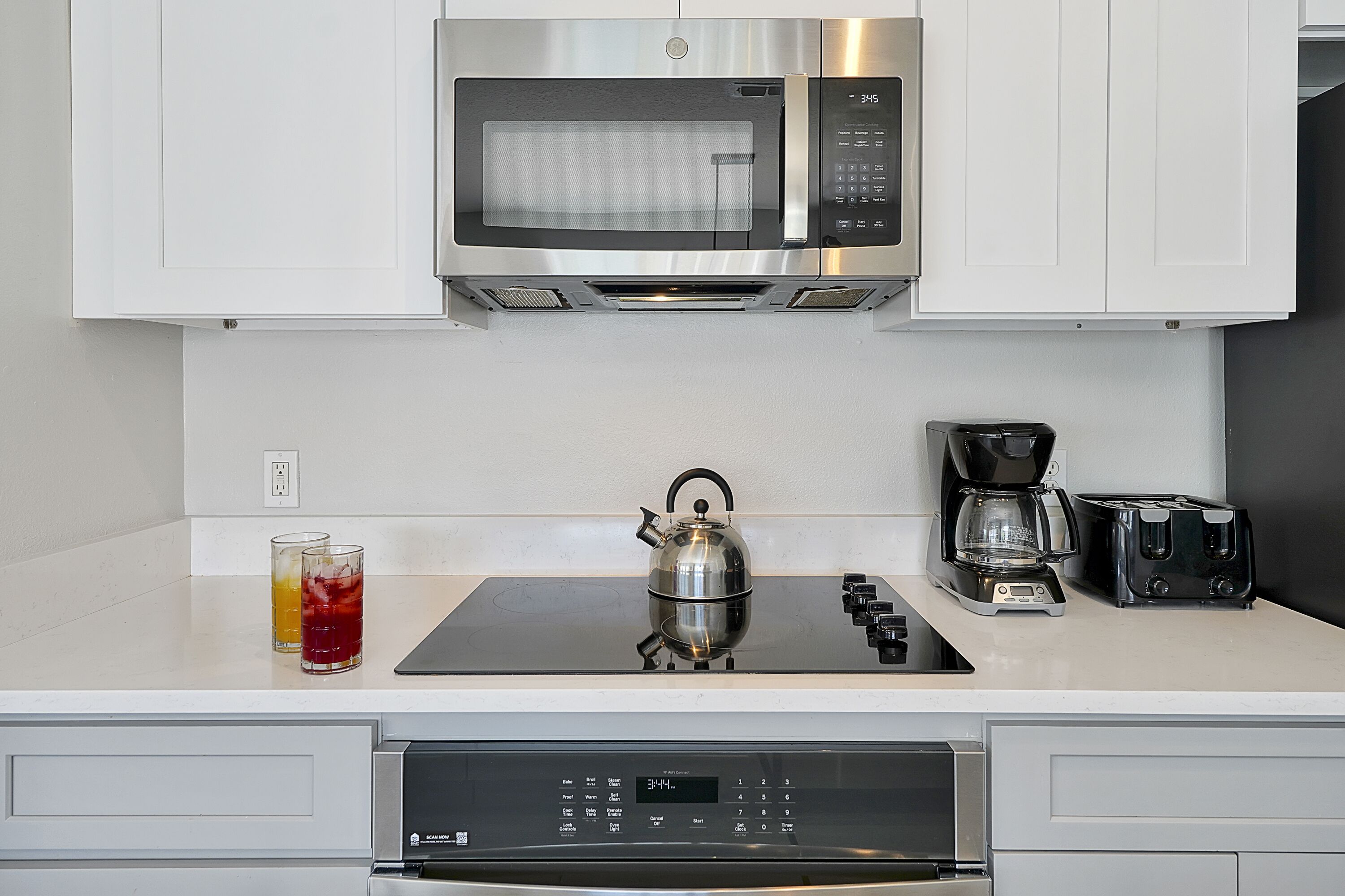 A modern kitchen with a built-in microwave, a kettle, a coffee maker, and a toaster on the countertop.