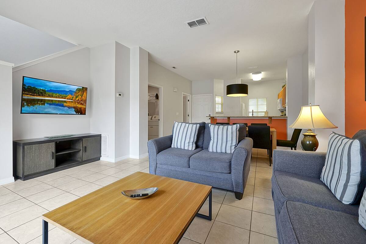 Ein modernes Wohnzimmer mit grauem Sofa, einem Holztisch und einem flachbildfernseher an der Wand.