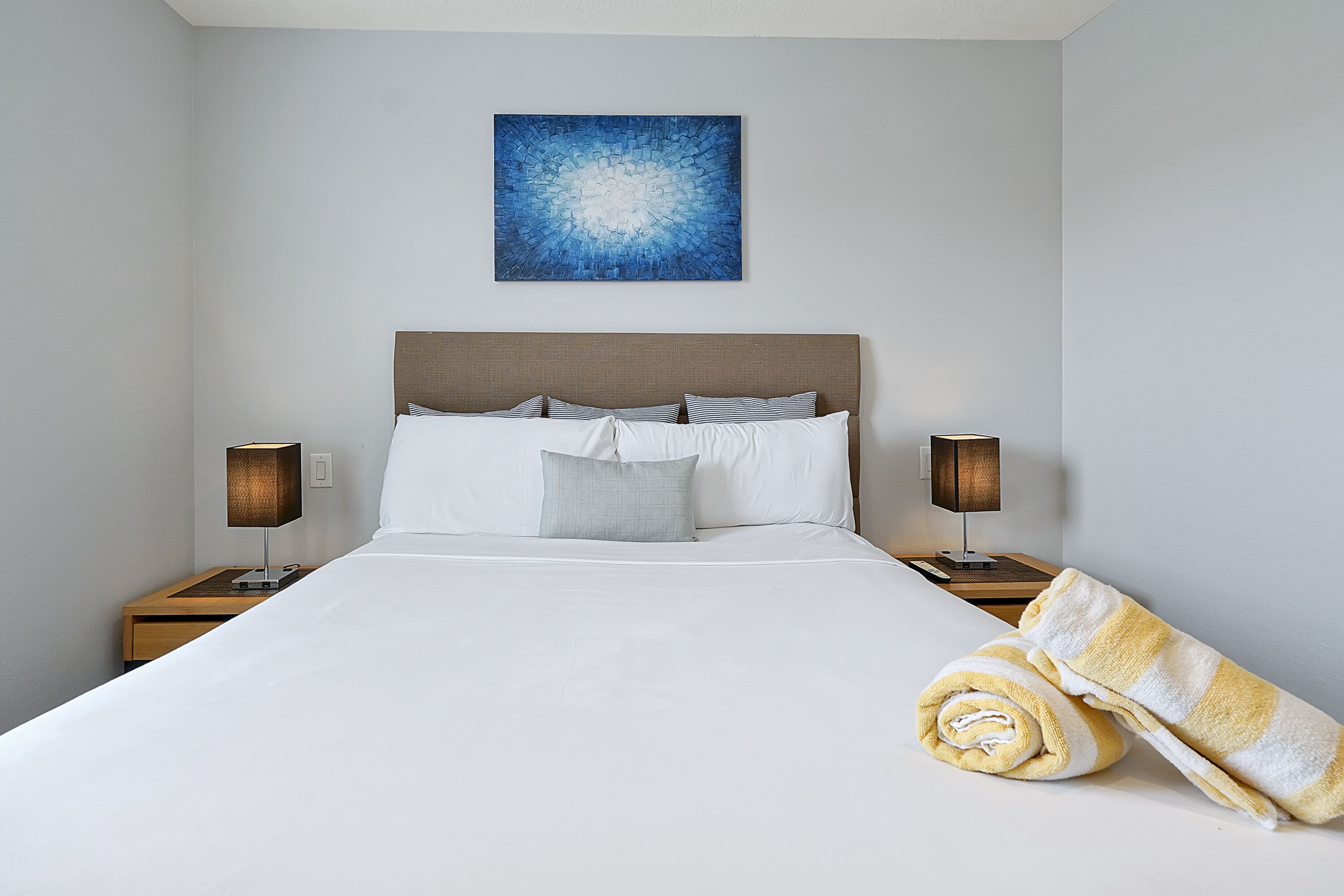 A neatly made bed with white linens, a headboard, and two bedside lamps.