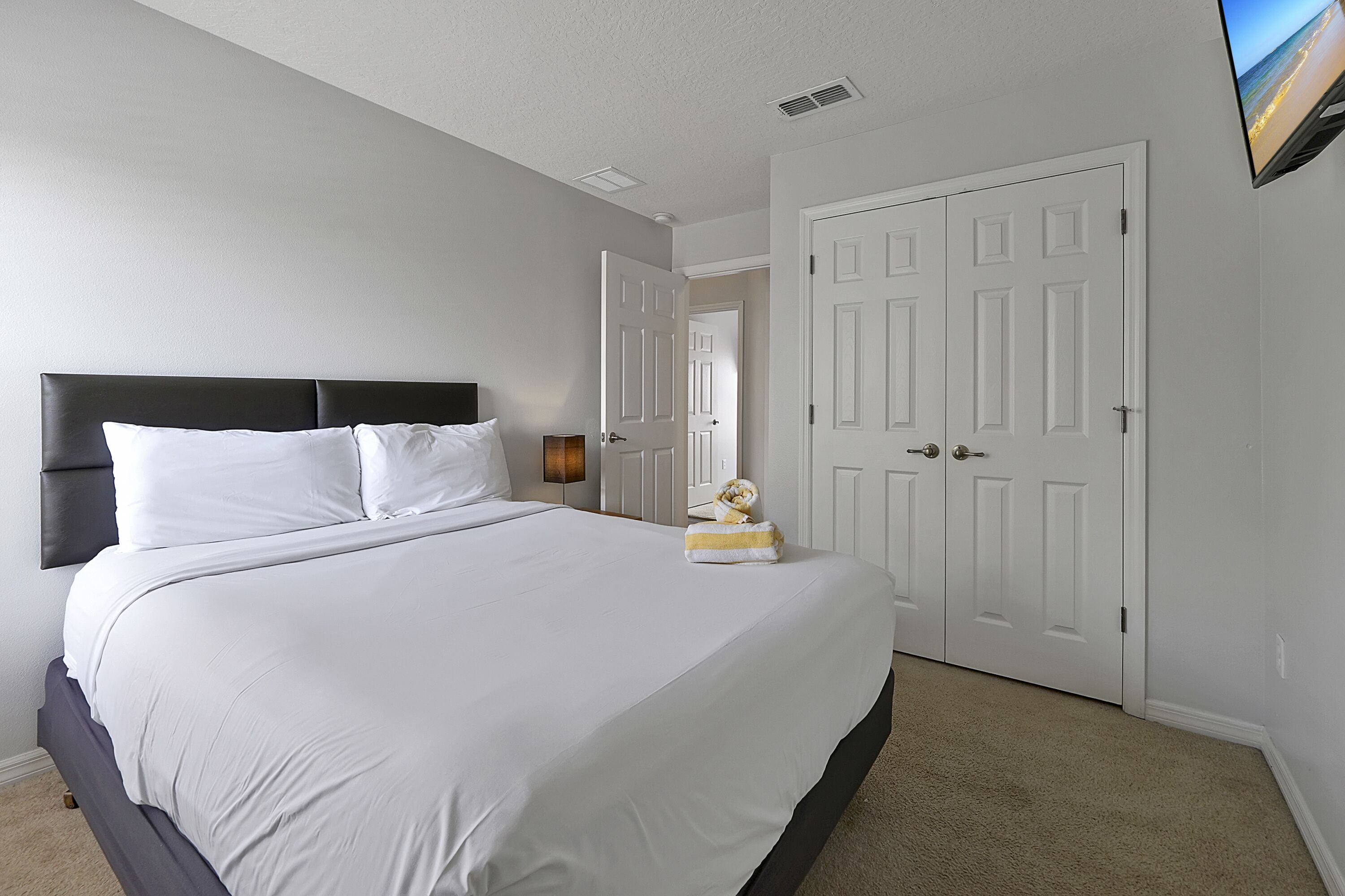 A neatly made bed with white linens and a dark headboard, a white door with a handle, and a flat-screen TV mounted on the wall.