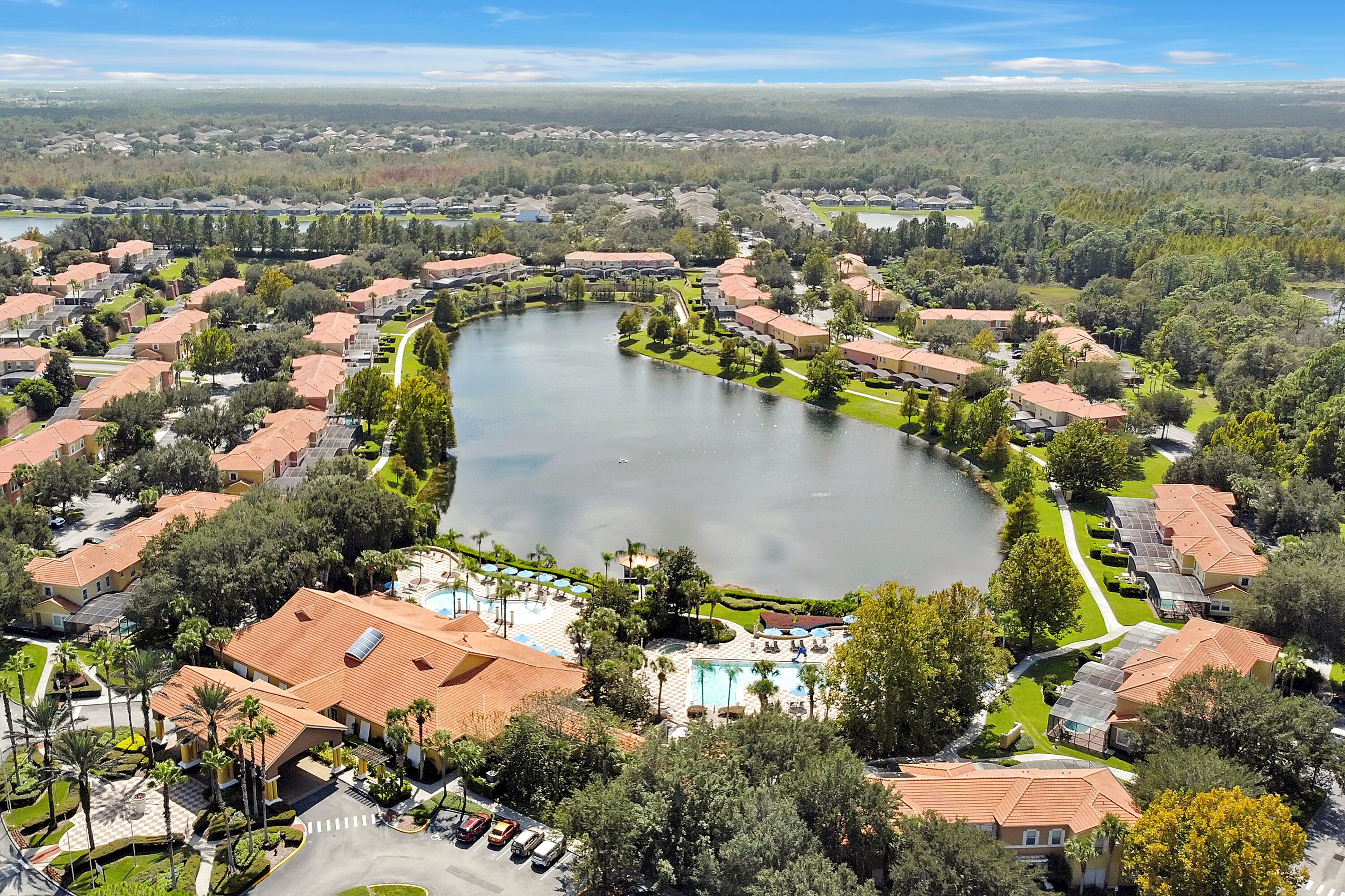 Vue aérienne d’un quartier résidentiel avec un grand lac, entouré de maisons aux toits rouges, et d’un espace piscine.