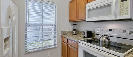 A kitchen with wooden cabinets, a microwave, a stove, and a window with blinds.
