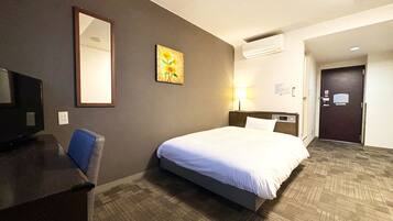 A hotel room with a bed, a desk, a chair, a mirror, a painting, a lamp, and a door.
