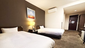Une chambre d’hôtel avec deux lits, une table de chevet avec une lampe, un appareil de climatisation et une porte donnant sur le couloir.