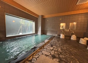 Un área de spa con suelo de baldosas de piedra, un ventanal grande y una pequeña piscina.