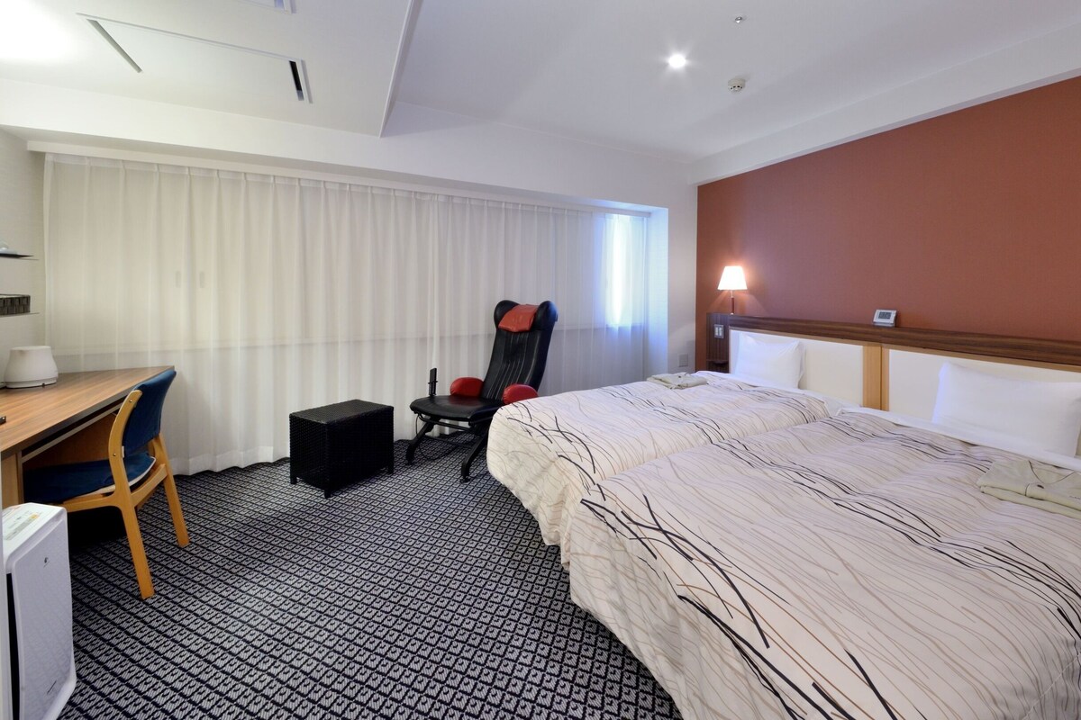 A hotel room with a bed, desk, chair, and a small table.