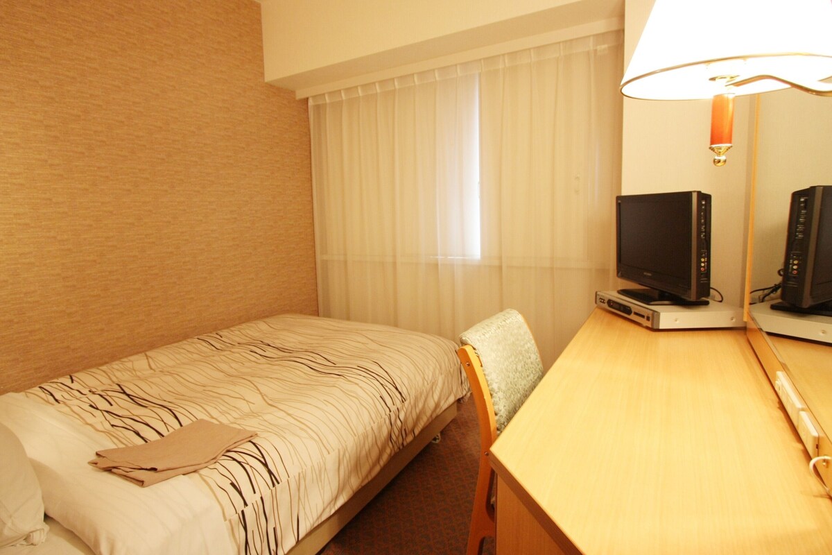 A hotel room with a single bed, a desk with a computer, and a television.