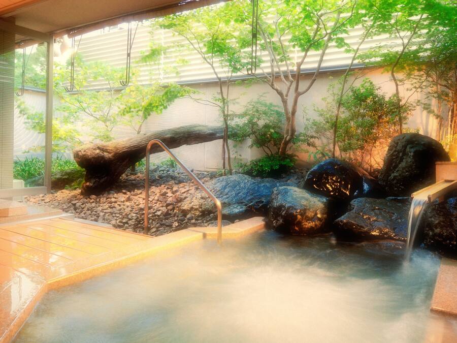 A hot spring area with a stone bench, a small waterfall, and a wooden bridge.