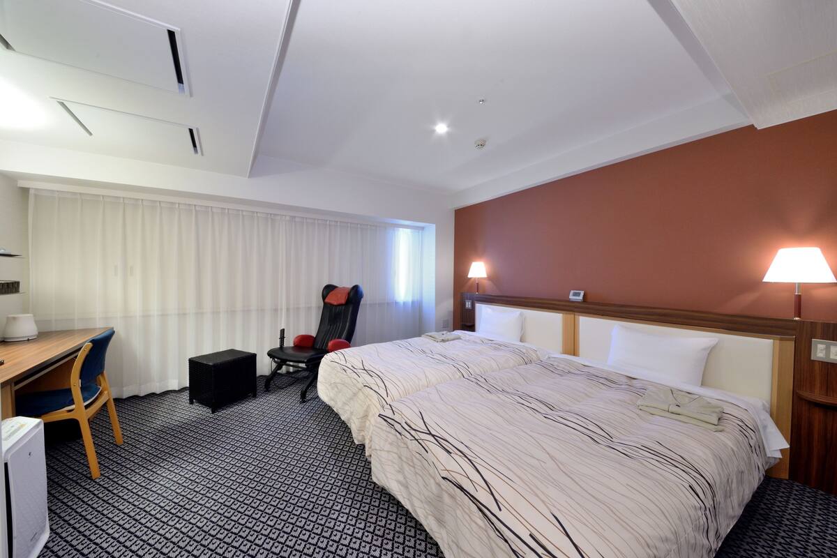 A hotel room with a bed, a desk, a chair, and a window with curtains.
