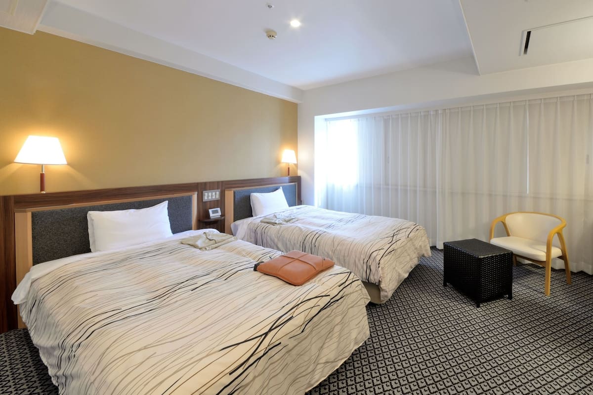 A hotel room with two beds, a desk, a chair, and a window with curtains.
