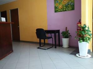 A room with a wooden desk, a black chair, a white potted plant, and a painting on the wall. - Zass Hotel (Kuala Lumpur)