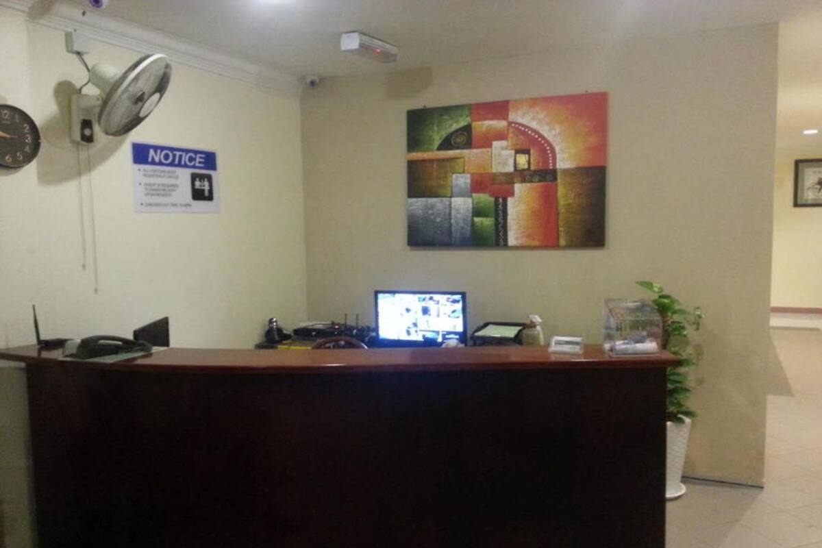 A reception desk with a computer monitor, a notice sign, a clock, and a potted plant.