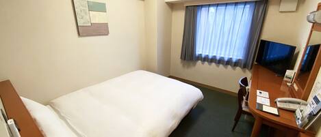 Una habitación de hotel con una cama individual, un escritorio con teléfono, un televisor y una ventana con cortinas.