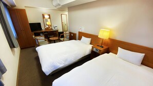 Habitación de hotel con dos camas, un escritorio con silla, una lámpara y un televisor.