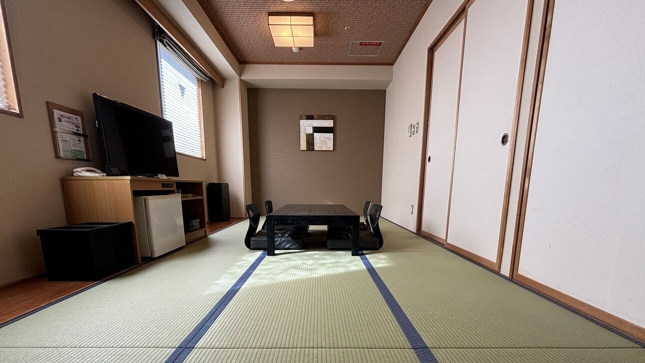 A traditional Japanese room with tatami flooring, a television, a small refrigerator, and a sliding door.