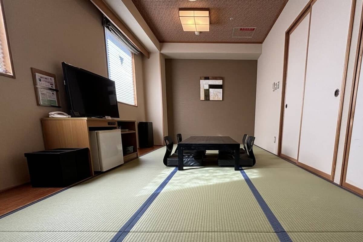 Une pièce de style japonais traditionnel, avec un sol recouvert de tatamis, une télévision, un petit réfrigérateur et une porte coulissante.