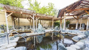 Un onsen japonais traditionnel, avec des bains en pierre, des structures en bois et un mur de pierre.