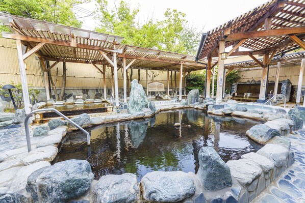 A traditional Japanese onsen with stone baths, wooden structures, and a stone wall. - Route Inn Grantia Hanyu Spa Resort (Hanyu)