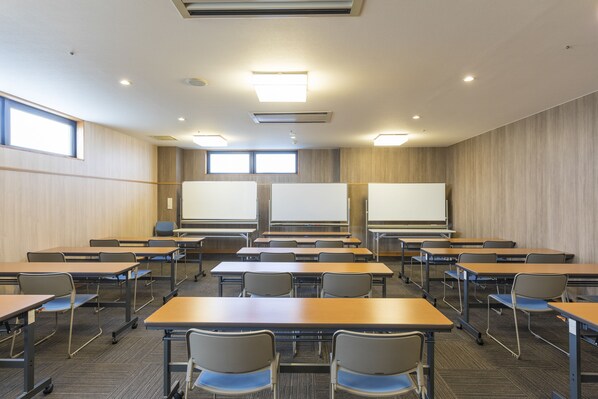 A classroom with desks, chairs, a projector screen, and a large window.