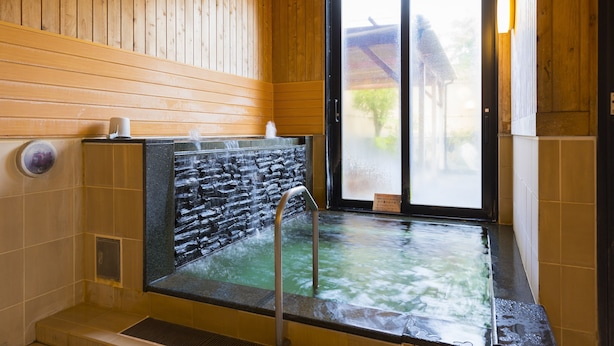 Un intérieur en bois avec un bain à eau chaude, un mur en pierre et une vue à travers une porte en verre.