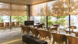 Un hall d’hôtel moderne avec de grandes fenêtres, des meubles en osier et un téléviseur à écran plat.