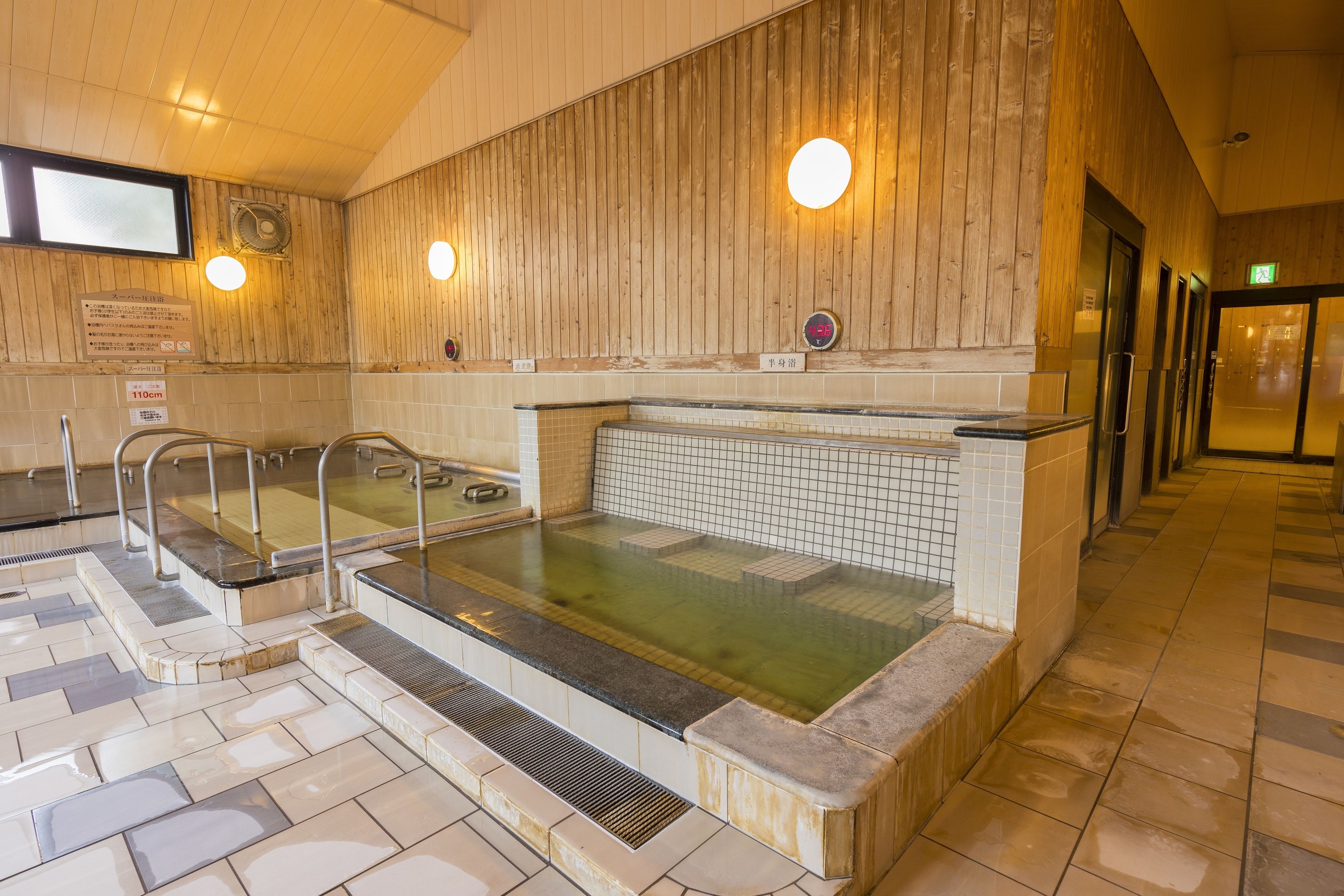 A traditional Japanese onsen with wooden walls, a tiled floor, and a stone bench.