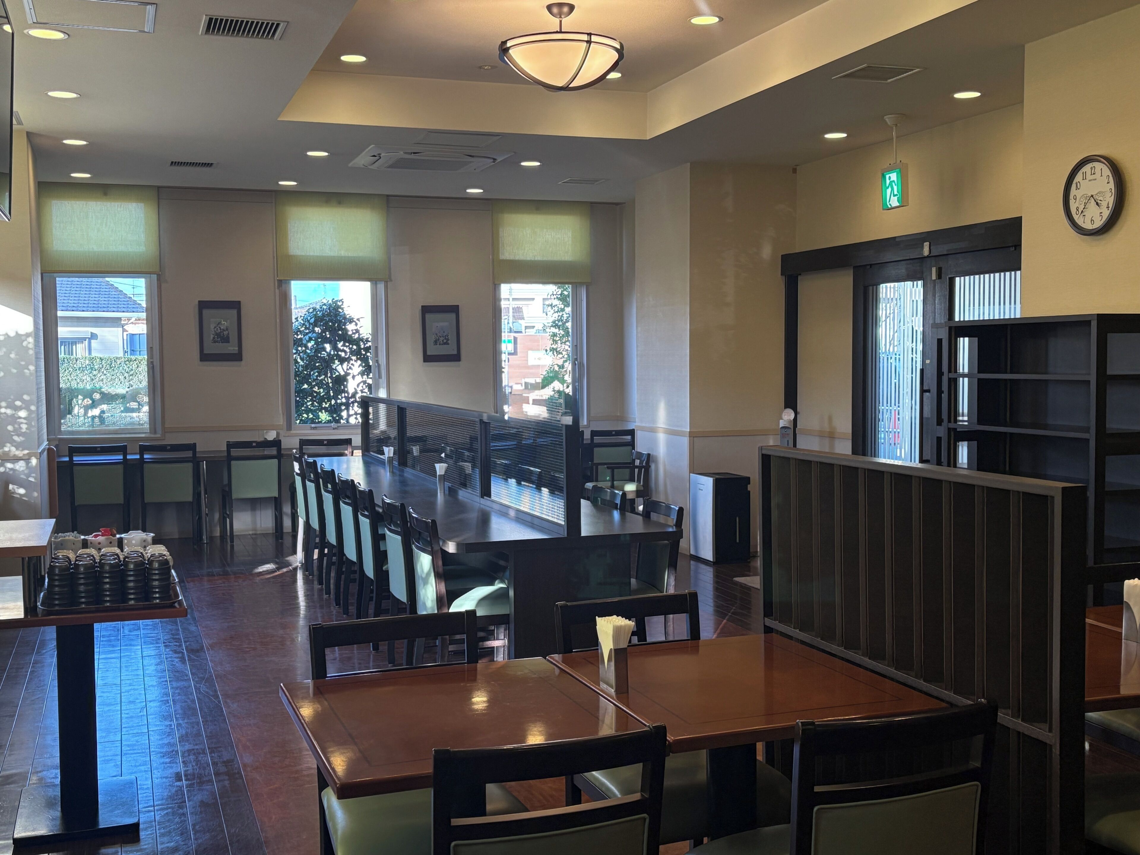 A restaurant interior with long communal tables, individual booths, and a view of the outdoors.