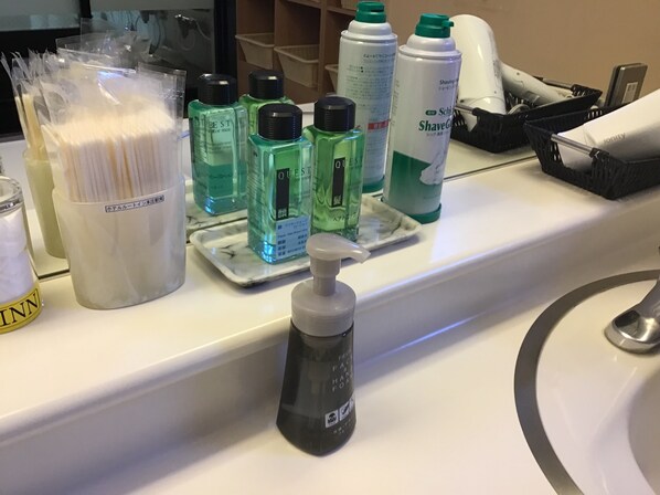 A bathroom counter with toiletries including a bottle of facial foam, several bottles of men's grooming products, and a container of cotton swabs. - Hotel Route Inn Honjo Ekiminami (Honjo)
