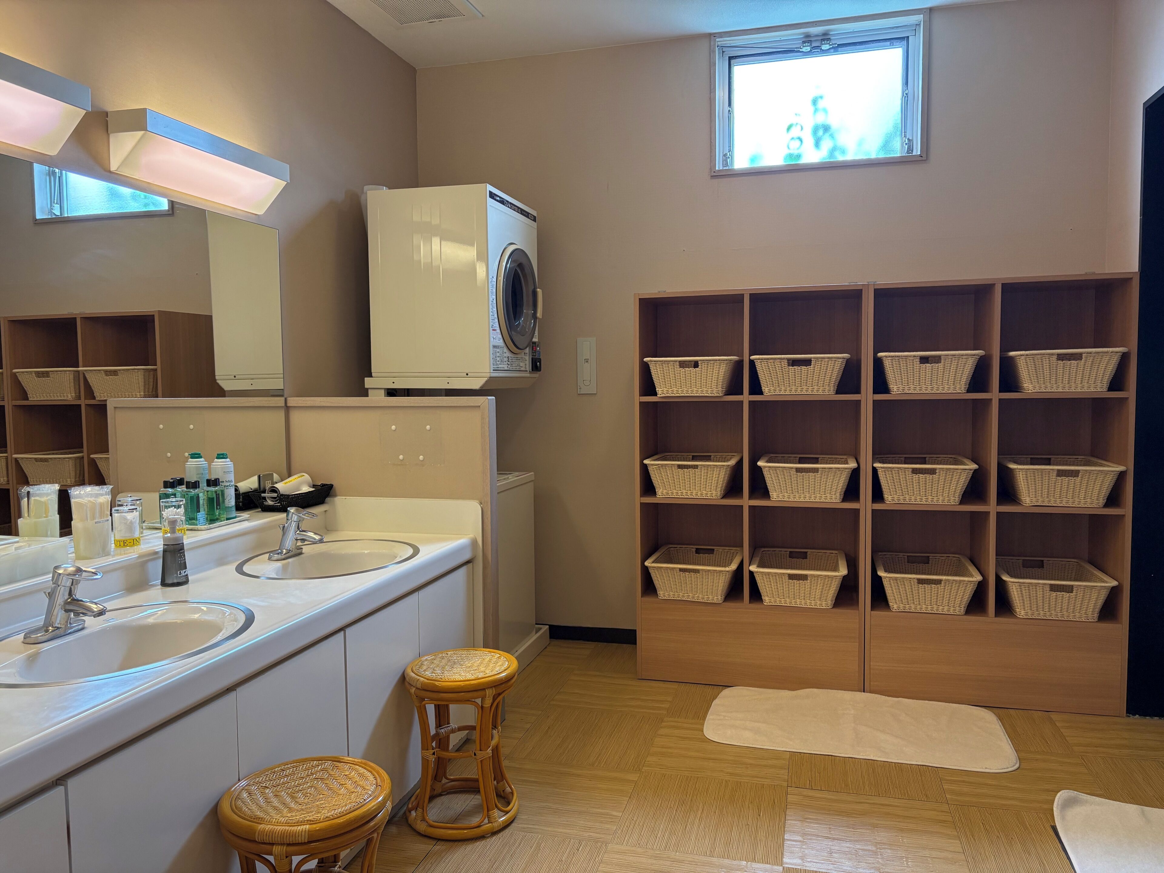 A bathroom with a washing machine, two sinks, wicker baskets, and a window.