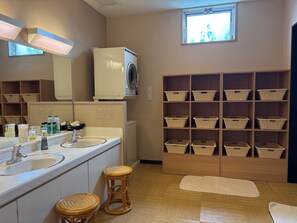 Une salle de bain équipée d’un lave-linge, de deux éviers, de paniers en osier et d’une fenêtre.