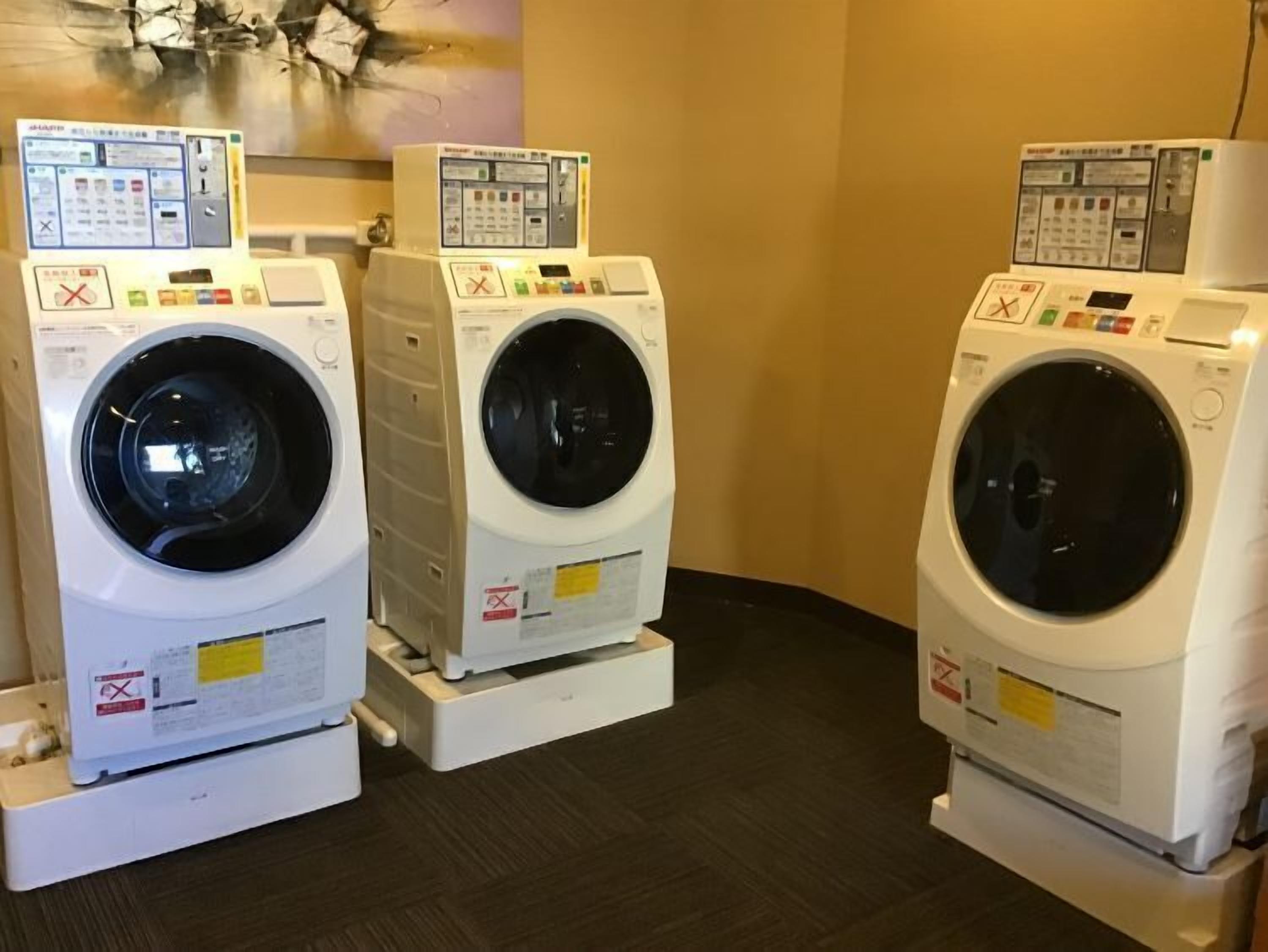 Three front-loading washing machines in a room with a dark floor and beige walls.
