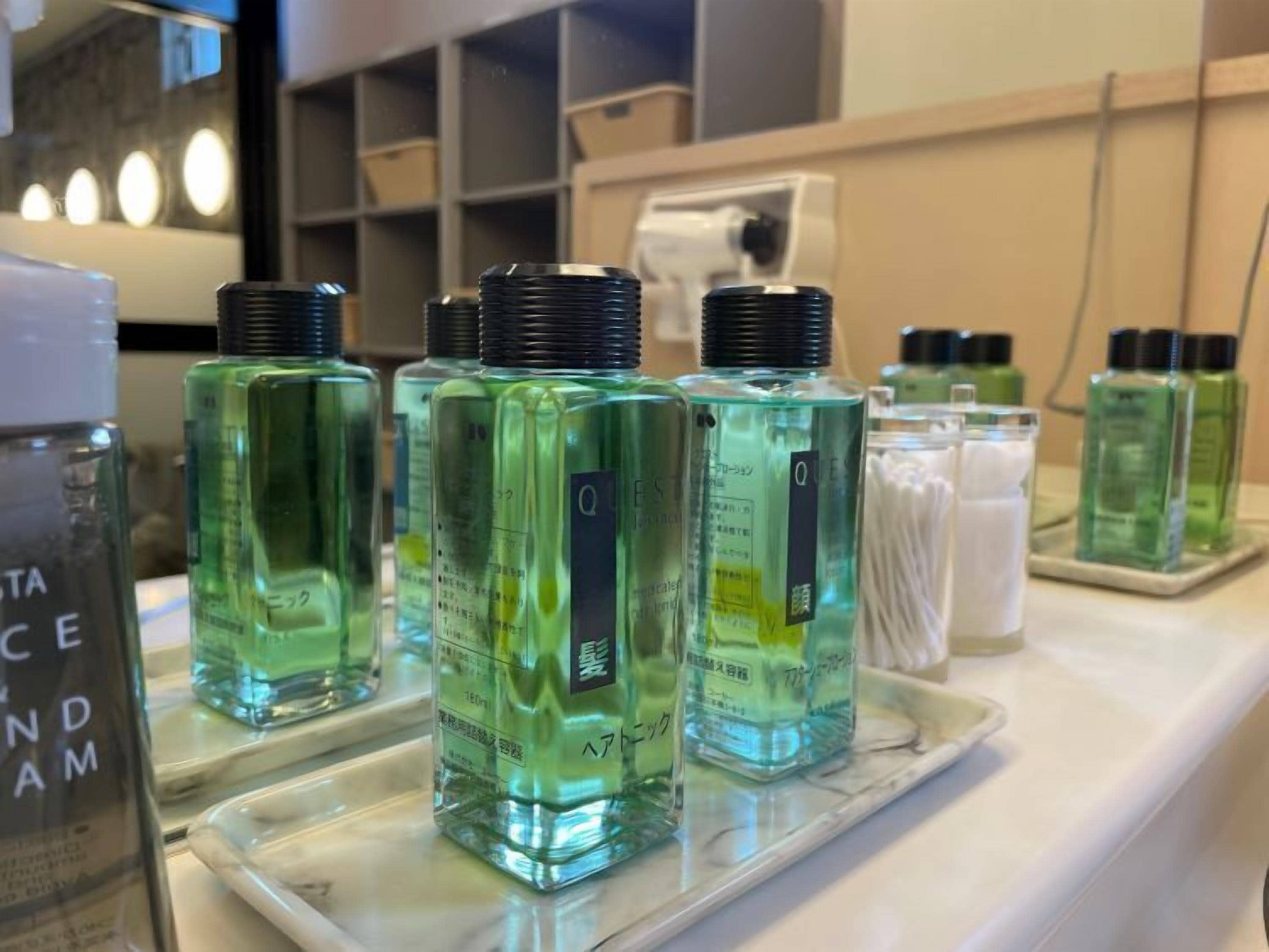 A display of green bottles on a marble countertop, likely containing personal care products.