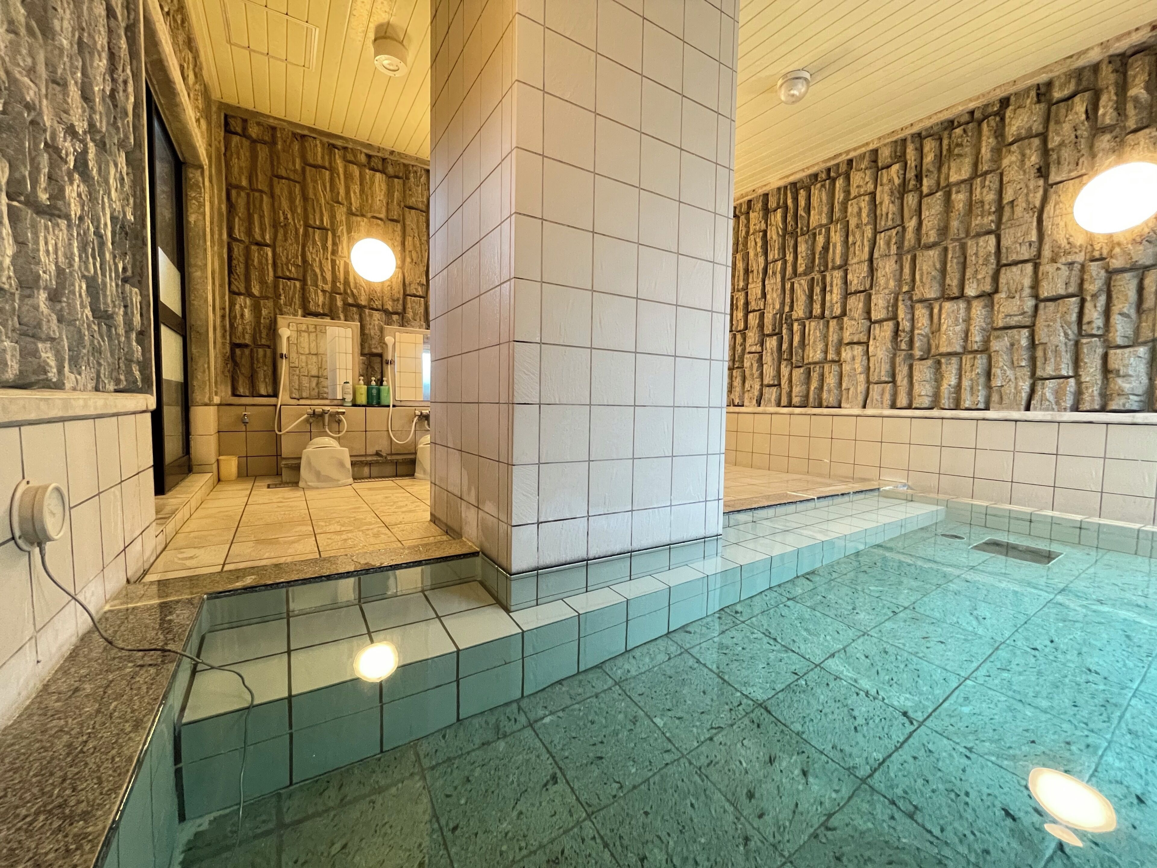 Ett spaområde med en stenmur, ett kaklat golv och en pool med glasväggar.