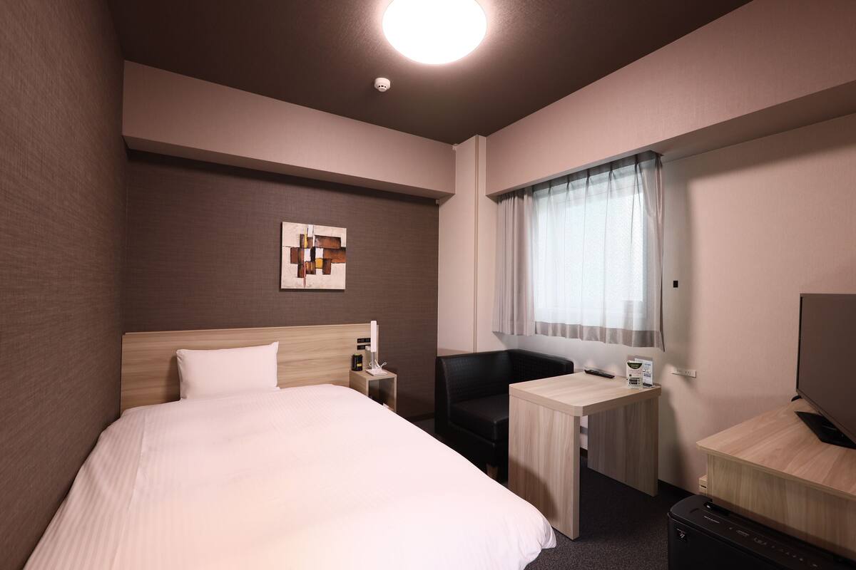 A hotel room with a large bed, a desk, a chair, a television, and a window with curtains.