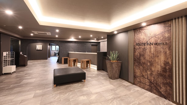 Un moderno vestíbulo de hotel con mostrador de recepción, zona de estar y una gran planta en maceta.