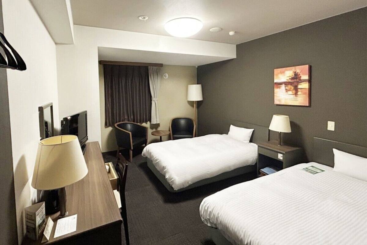 A hotel room with two beds, a desk, a chair, a TV, and a painting on the wall.