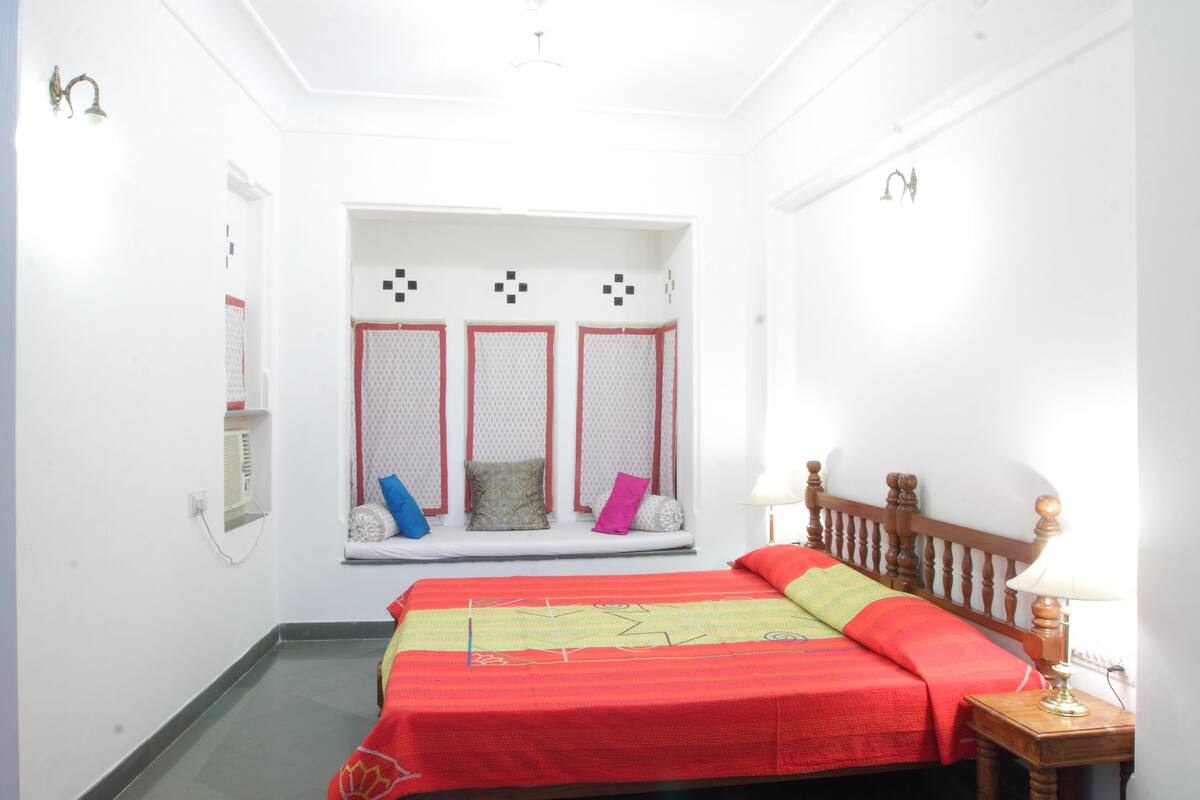 Un dormitorio con cama, ventana con vistas, mesita de noche y aire acondicionado instalado en la pared.