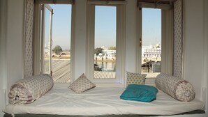 A room with a bed, three windows, and a view of a building across a body of water.