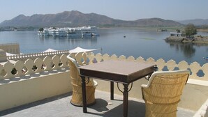 A terrace with a table and chairs overlooking a lake with boats and hills in the background.