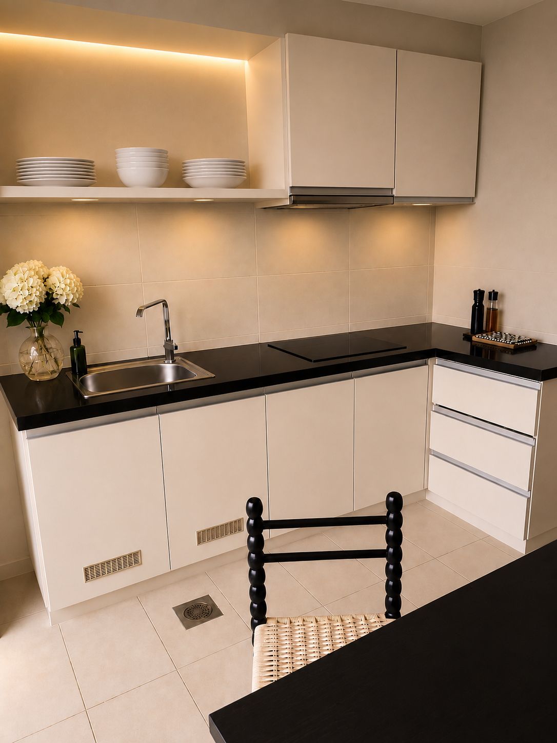 A modern kitchen with a black countertop, white cabinets, a stainless steel sink, and a chair with a woven seat.