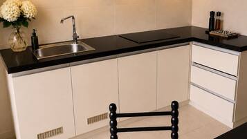 A modern kitchen with a black countertop, white cabinets, a stainless steel sink, and a chair with a woven seat.