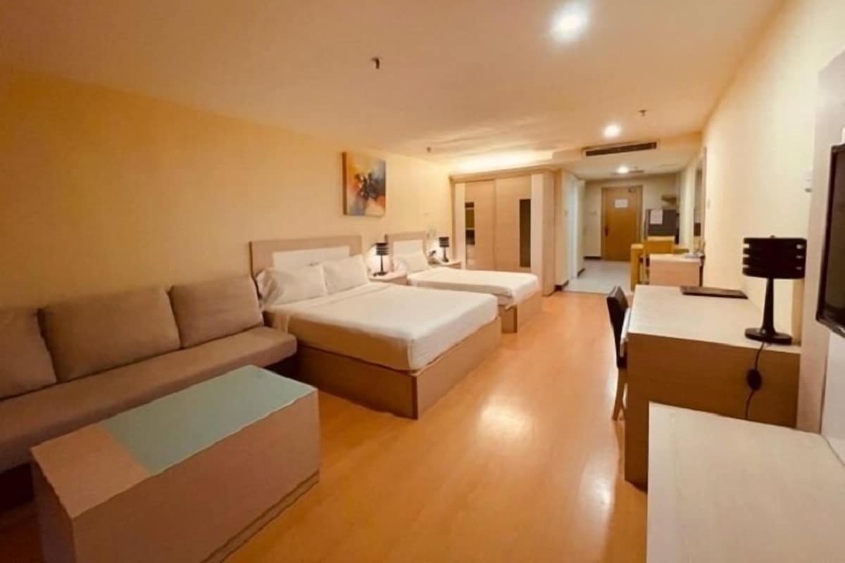 A hotel room with a sofa, two beds, a desk, and a TV.