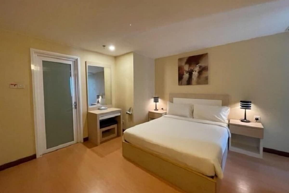 A hotel room with a bed, bedside tables, a mirror, and a wall-mounted artwork.