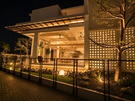Un edificio moderno con un área exterior cubierta, un muro decorativo con diseños circulares y un jardín bien cuidado con rocas y plantas.